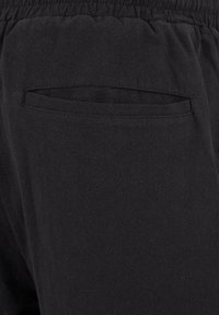 Gros plan sur un pantalon en tissu noir avec une ceinture élastique et une poche fendue horizontale au dos.