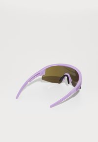 Lunettes de soleil violettes au design englobant, dotées de verres teintés marron et de temples flexibles. Marquage notable sur la monture.