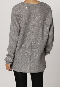 Vaaleanharmaa neulepaita, jossa on väljä leikkaus, neulottu pintakuvio, paljettiyksityiskohdat, pudotetut olkaimet ja keskisauma takana.