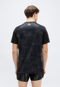 Μαύρο αθλητικό μπλουζάκι με υφή και σχέδιο στην πλάτη. Κοντά μανίκια και ριμπ λεπτομέρειες στους ώμους. Διαθέτει μικρό χρυσό λογότυπο στο πάνω μέρος της πλάτης.