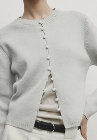 Vaaleanharmaa neulottu neuletakki pyöreällä pääntiellä, jossa etupuolella kangaspäällysteiset napit ja resorilla viimeistellyt hihansuut.