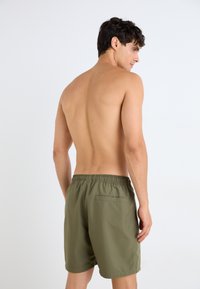 Olivegrønne badetights laget av lett, hurtigtørkende stoff, med elastisk midje og en baklomme.