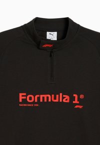 Mustapintainen fleecetakki, jossa on neljännesvetoketju, jossa on näkyvästi punainen "Formula 1" -teksti ja logo rinnan kohdalla. Teksturoitu kangas ja korkea kaulus.
