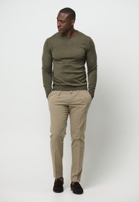Suéter de punto oliva de corte ajustado combinado con pantalones beige y mocasines marrón oscuro. Textura suave y diseño minimalista.