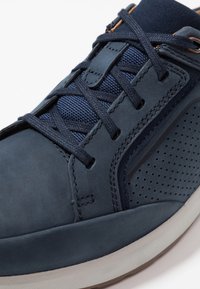 Marinblå sneakers med en kombination av läder och mesh, med sydda detaljer, en strukturerad yta och perforerade detaljer på sidan.