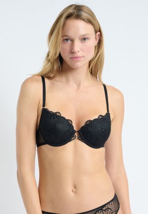 Reggiseno nero con ferretto, dettagli in pizzo, bordi ondulati e spalline regolabili. Presenta un piccolo elemento decorativo al centro davanti.