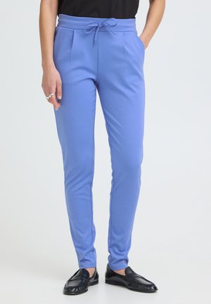 Slim-fit lyseblå bukser med snøre i taljen, sidelommer, båret med sorte loafers på en person mod en ensfarvet baggrund.
