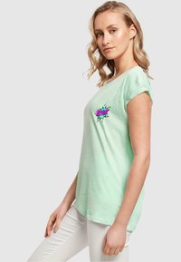 Lys mintgrøn kortærmet t-shirt med en farverig "BOOM!" grafik på brystet. Blødt stof med en afslappet pasform og opkrøllede ærmer.