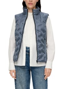 Gepolsterte graue Weste mit hohem Kragen, Reißverschluss und seitlichen Taschen, über einem weißen Hemd mit Knöpfen getragen, kombiniert mit blauen Jeans.