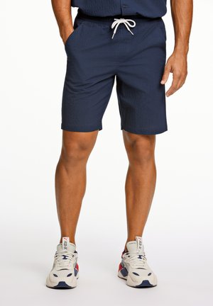 Mørkeblå shorts i et tekstureret materiale med elastisk talje og snøre. Har sidelommer og en knælængde.