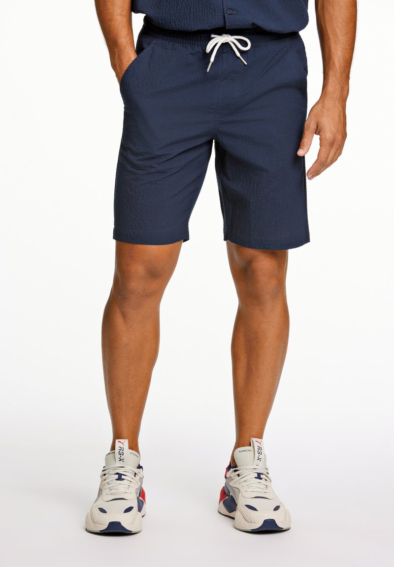 Marina blå shorts i ett texturerat tyg med elastisk midja och dragsko. Har sidofickor och en knälång längd.