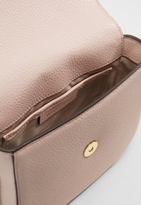 Indvendig i en lyserød struktureret lædertaske med en gylden, cirkulær hårdvaredetalje. Har en lille lomme og glat foret.