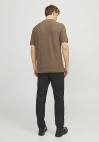 Polo shirt marrone a maniche corte con una finitura testurizzata, abbinato a pantaloni neri e calzature scure, visto da dietro.