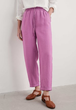 Pantalons légers avec taille élastique en lin rose vif. Présentent une coupe décontractée, des poches latérales et un cordon de serrage. Portés avec des chaussures tissées marron.