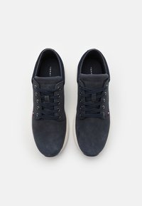 Mörkblå sneakers med texturerad mocka ovandel, rund tå och vit gummisula. Har sex hål för snörning och logotyp på tungan och sidan.
