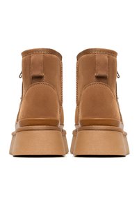 Braune Wildleder-Ankle- Boots mit einer dicken Plateausohle, runder Zehenform, glatten Nähten und Zuglaschen an der Rückseite.