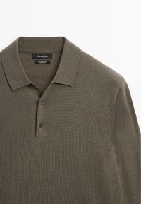 Olive green wool polo shirt with a ribbed texture, featuring a three-button placket and a classic collar. Brand label visible.