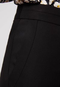 Pantalons noirs ajustés en tissu lisse et mat, avec des coutures structurées et une taille haute pour une silhouette épurée.