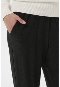 Melnas, spīdīgas bikses ar sānu kabatām. Audums ir gluds un ar vieglu spīdumu. Virs vidukļa ar ribotu baltu jostu.