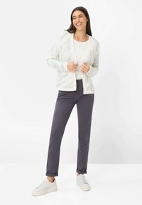 Let cardigan med mønster i creme og grå, kombineret med grå bukser og hvide sneakers. Cardiganen har åben front og ribstrikkede ærmekanter.