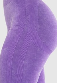Leggings viola con una finitura testurizzata, dotati di pannelli a costine e lisci, progettati per una vestibilità perfetta. I dettagli enfatizzano la forma e il movimento.