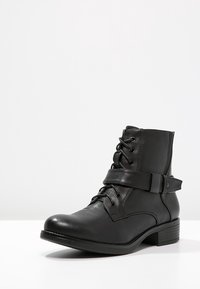 Stivale alla caviglia in pelle nera con allacciatura frontale, cinturino regolabile e tacco a blocco small. Texture liscia con dettagli hardware minimi.