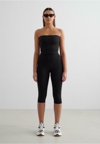 Black strapless top paired with high-waisted black leggings, featuring a smooth texture. Completed with white and black athletic shoes.