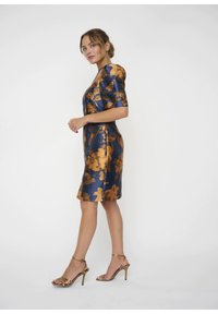Blaues Satin-Kleid mit goldenen Blumenmuster, kurzen Ärmeln, figurbetontem Schnitt, knielang, kombiniert mit goldenen, rückenfreien High Heels.