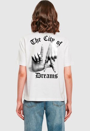 Valkoinen puuvillateeppari, jossa on musta graafinen kuvasto käsistä, jotka muodostavat kirjaimia, tekstillä "The City of Dreams" yläpuolella.