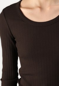 Dunkelbraunes geripptes Langarmoberteil mit weitem Rundhalsausschnitt. Weicher Stoff mit figurnaher Passform und subtilen Nähten.