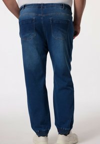 Joggers de mezclilla azul oscuro con cinturilla elástica, dos bolsillos traseros y puños elásticos en los tobillos, mostrados desde la parte de atrás.