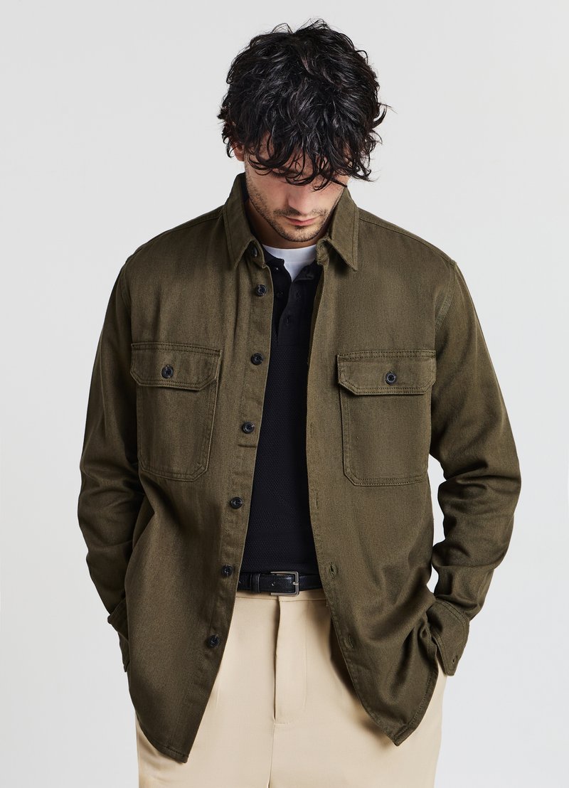 Camicia verde oliva con bottoni realizzata in tessuto morbido, caratterizzata da due tasche a toppa con pattine a bottone, colletto classico e vestibilità comoda.