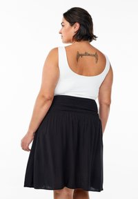 Haut sans manches blanc associé à une jupe noire mi-longue dotée d'une ceinture élastique et d'une texture de tissu lisse et fluide.