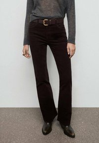 Pantalones acampanados de corduroy burdeos con cintura ajustada, que incluyen trabillas para cinturón, combinados con un suéter gris y botas negras hasta el tobillo.