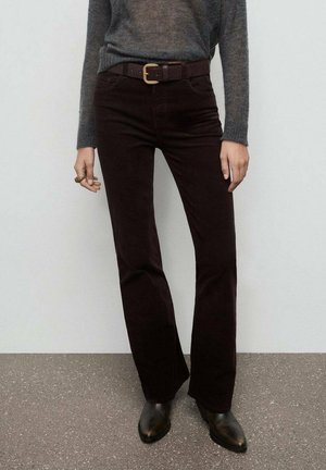 Pantalones acampanados de corduroy burdeos con cintura ajustada, que incluyen trabillas para cinturón, combinados con un suéter gris y botas negras hasta el tobillo.
