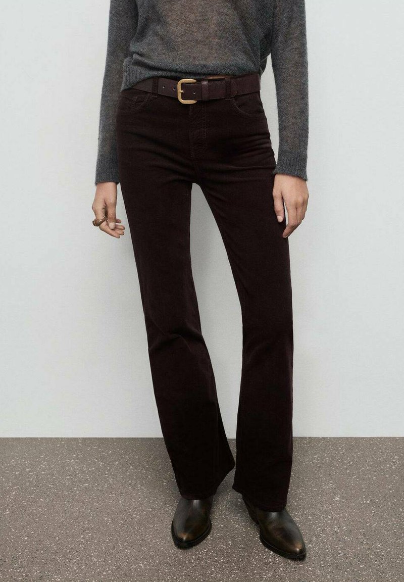 Pantalones acampanados de corduroy burdeos con cintura ajustada, que incluyen trabillas para cinturón, combinados con un suéter gris y botas negras hasta el tobillo.