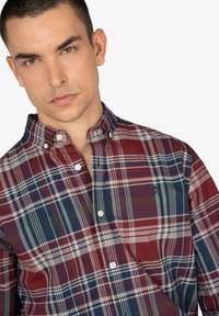 Camisa de cuadros de botones en rojo, azul marino y verde. Presenta un collar clásico, bolsillo frontal y botones blancos. Tejido de algodón con una textura suave.