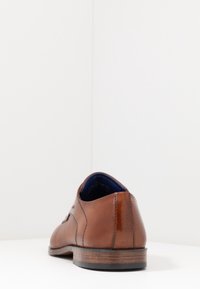 Chaussure en cuir marron à finition lisse, côté légèrement texturé et semelle en bois. Présente une doublure bleue et des détails de couture minimalistes.