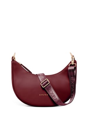 Burgunderrote, halbmondförmige Handtasche mit goldfarbener Hardware, verstellbarem Logoriemen und goldenem „Expatrié“-Print auf der Vorderseite.