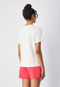 Witte katoenen t-shirt met korte opgerolde mouwen, met een klassieke ronde halslijn. Draag het met felroze shorts. Minimalistisch ontwerp, geen patronen.