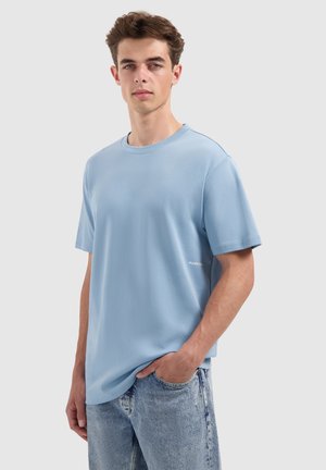 Hellblaues Baumwoll-T-Shirt mit lässiger Passform, kurzen Ärmeln und Rundhalsausschnitt. Mit einem kleinen weißen Logodetail nahe dem Saum.