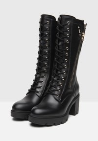 Black leather knee-high boots with a lace-up front, gold eyelets, and side zipper. Chunky heel and textured sole for added grip.