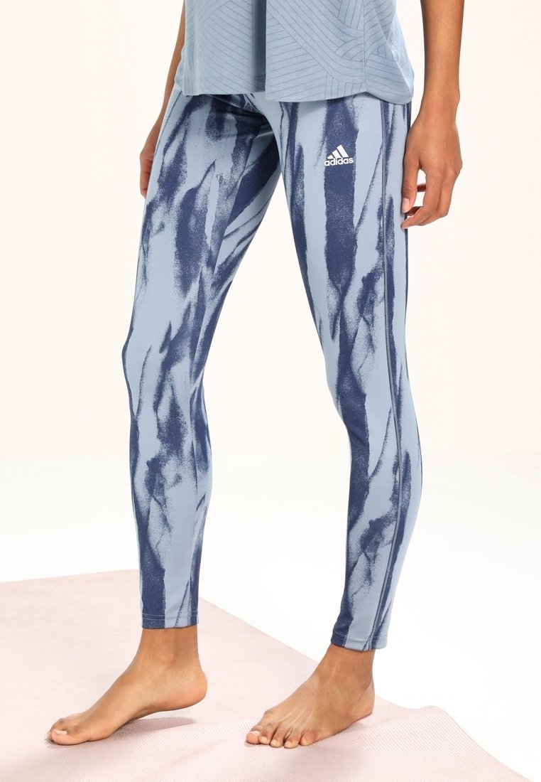 Adidas naisten legginssit vaaleansinisinä, joissa on tummansinisiä abstrakteja viivoja, joustavasta materiaalista valmistettu, tiukka istuvuus ja logo sivussa.