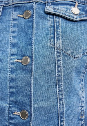 Jeansjacke aus hellblauem Stoff, fünf silberne Knöpfe, Nähdetails und eine einzelne Brusttasche. Die Textur ist leicht abgenutzt.