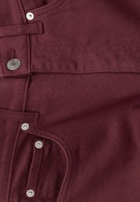 Burgundy fabric with a smooth texture, featuring silver snaps, a front pocket, and stitched seams, highlighting a structured design.