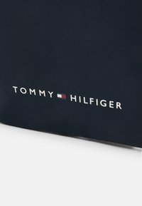 Borsa Tommy Hilfiger blu navy con texture liscia, caratterizzata da un logo in testo bianco con accenti rossi e blu. Forma semplice e rettangolare.