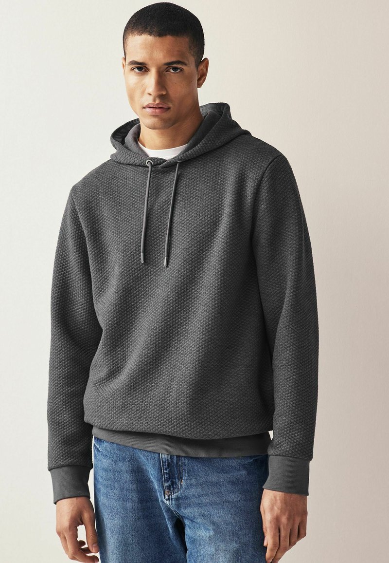 Grå tekstureret hoodie med snøre hætte, forret indeni og ribbede manchetter. Iført med lyseblå denim jeans.