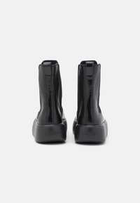 Botines negros hasta el tobillo con acabado brillante, paneles laterales elásticos, suela negra texturizada y un logo sutil de la marca en la parte trasera.