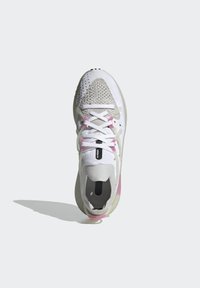 White athletic shoe featuring a knitted upper, grey accents, pink detailing on the heel, and a textured sole with black grips.