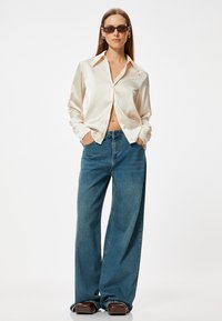 Zijdeachtige, off-white blouse met een kraag en knoopsluiting, gecombineerd met wijde, lichtblauwe denim jeans en bruine platform schoenen.
